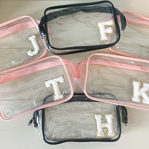 May include: Six clear plastic zippered pouches with pink and black trim. Each pouch has a white fluffy letter on the front: J, F, T, K, H, H.