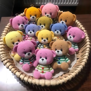 Può includere: Una collezione di portachiavi a forma di orsacchiotto all'uncinetto in vari colori, tra cui rosa, giallo, blu, verde, marrone e arancione. Gli orsacchiotti sono tutti seduti in un cesto di vimini.