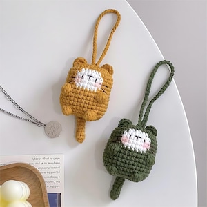 May include: Two crocheted cat keychains, one yellow and one green, with white faces and pink cheeks.