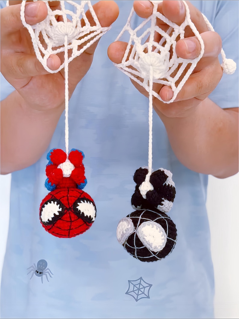 May include: Two crocheted figures hanging from white yarn strings attached to white crocheted web squares. One figure is red and blue with large white eyes, and the other is black and white with large white eyes, both featuring round heads.