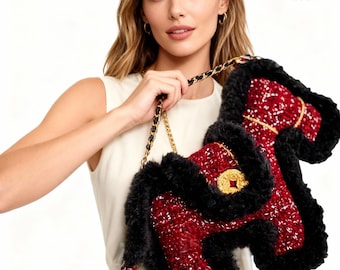 May include: A red and black handbag with a gold chain strap. The bag has a textured red body with black fur trim. A gold emblem is visible on the front. The bag is approximately 20 inches long.