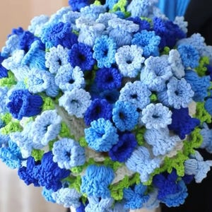 May include: A crocheted bouquet of blue and green flowers. The flowers are arranged in a white crocheted basket.