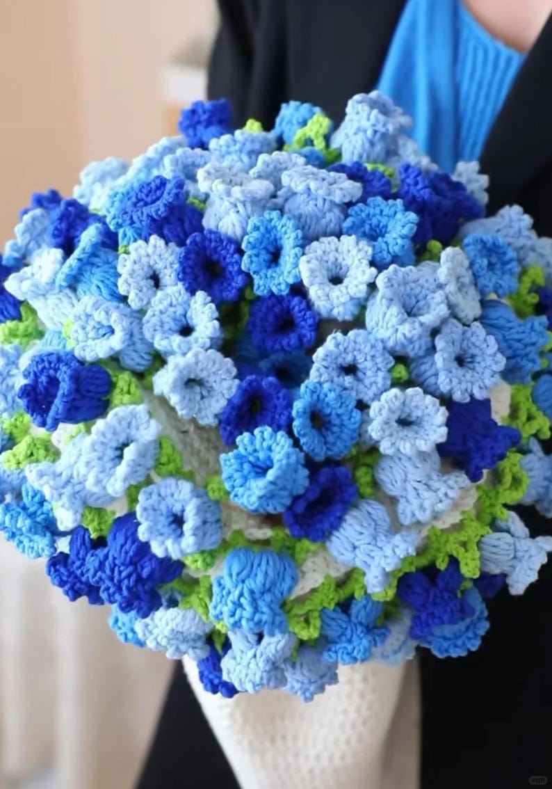May include: A crocheted bouquet of blue and green flowers. The flowers are arranged in a white crocheted basket.