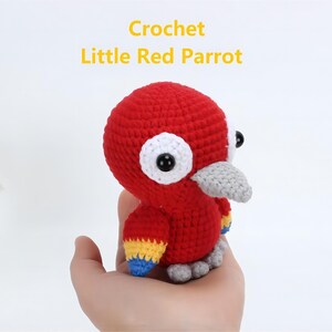 May include: A crocheted red parrot with yellow, blue, and white accents. The parrot has large white eyes with black pupils and a gray beak.