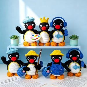 May include: A group of handmade crochet penguin dolls, each with unique accessories. The penguins are black, white, and orange, with various hats, crowns, and accessories like paint palettes, fishing rods, and headphones. The dolls are displayed on a white shelf.