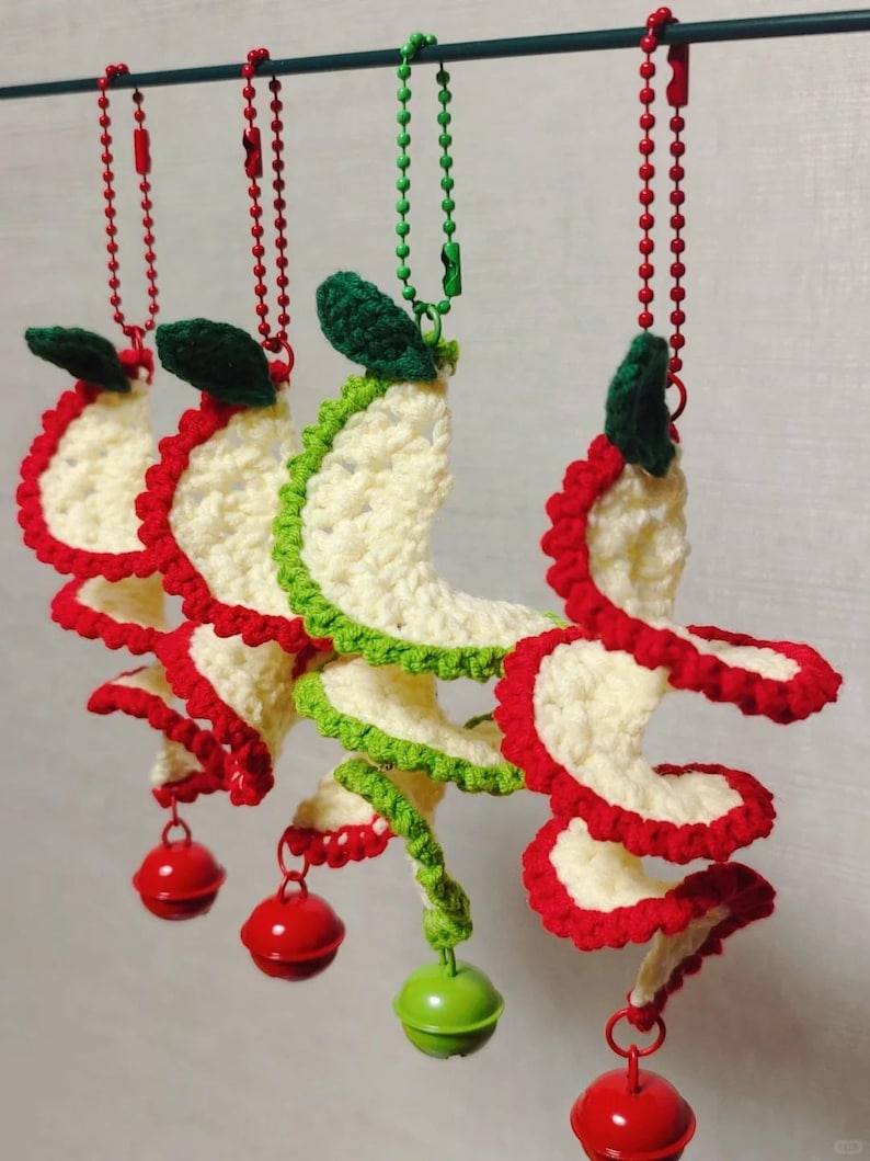 May include: Crocheted spiral ornaments in cream, red, and green, each with a small bell at the bottom. The ornaments are suspended from a metal bar by red and green beaded chains. The spiral design is reminiscent of a festive holiday decoration.