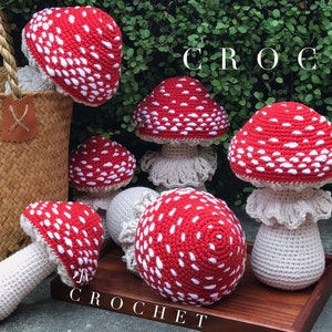 May include: Five crocheted red and white mushroom toys with white stems. The mushrooms are arranged on a wooden tray with the word "CROCHET" written on the tray.