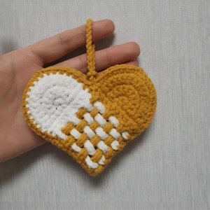 Peut inclure: Une d&eacute;coration en forme de c&oelig;ur crochet&eacute; avec un motif blanc et jaune. La d&eacute;coration a une boucle en haut pour l'accrocher.
