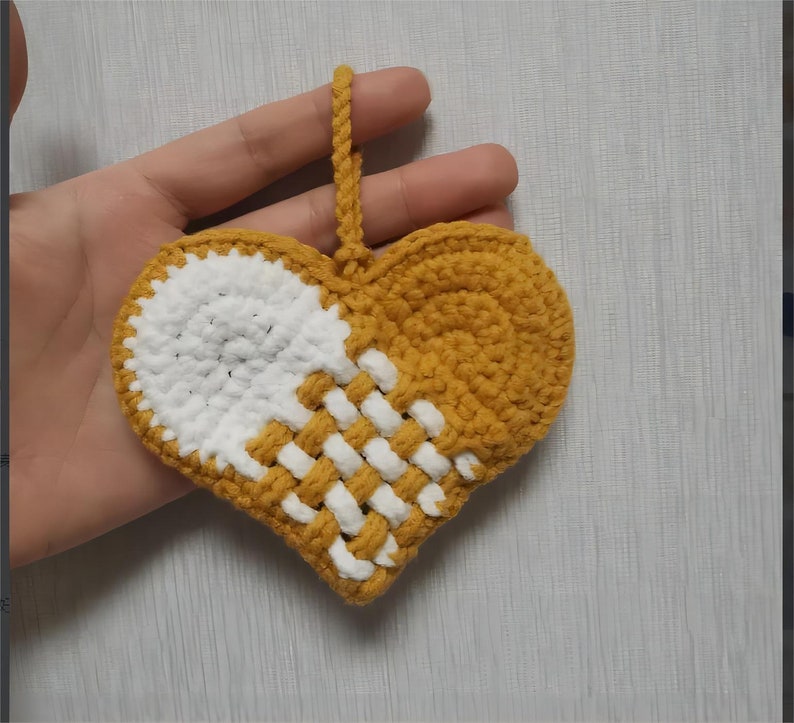 Peut inclure: Une d&eacute;coration en forme de c&oelig;ur crochet&eacute; avec un motif blanc et jaune. La d&eacute;coration a une boucle en haut pour l'accrocher.