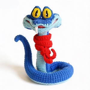 Peut inclure: Un jouet serpent en crochet bleu, avec un foulard rouge, de grands yeux jaunes et bleus et une dent blanche. Le serpent est enroulé, la tête relevée. Fait à la main.