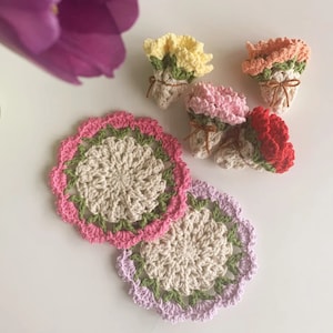 Puede incluir: Cuatro posavasos de ganchillo en forma de flor en rosa, rojo, amarillo y blanco. Los posavasos son redondos y tienen un delicado diseño de ganchillo.