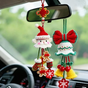 May include: Two handmade Christmas car charms hanging from a car's rearview mirror. One charm is Santa Claus, the other is a bell with a red bow. Both are crocheted in red, white, green, and yellow, with gingerbread men and snowflakes.
