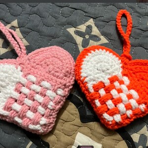 Peut inclure: Deux ornements en forme de c&oelig;ur en crochet, l'un rose et blanc, l'autre orange et blanc. Les deux ont un motif tiss&eacute; et une boucle pour accrocher.