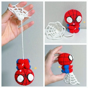 May include: A small, handmade crochet figure of a red and blue character with a round head, large white eyes, and black web-like stitching. The figure is attached to a white crocheted web strand and a circular web piece, showcasing its design.