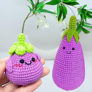 May include: Two crocheted purple eggplant plushies with green tops and smiling faces. The plushies are made with a textured yarn and have black eyes and a stitched smile.