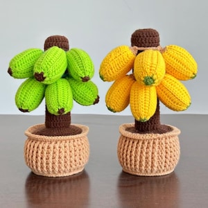 May include: Two crocheted banana plant decorations. One plant has green bananas and the other has yellow bananas. Both plants are in brown crocheted pots.