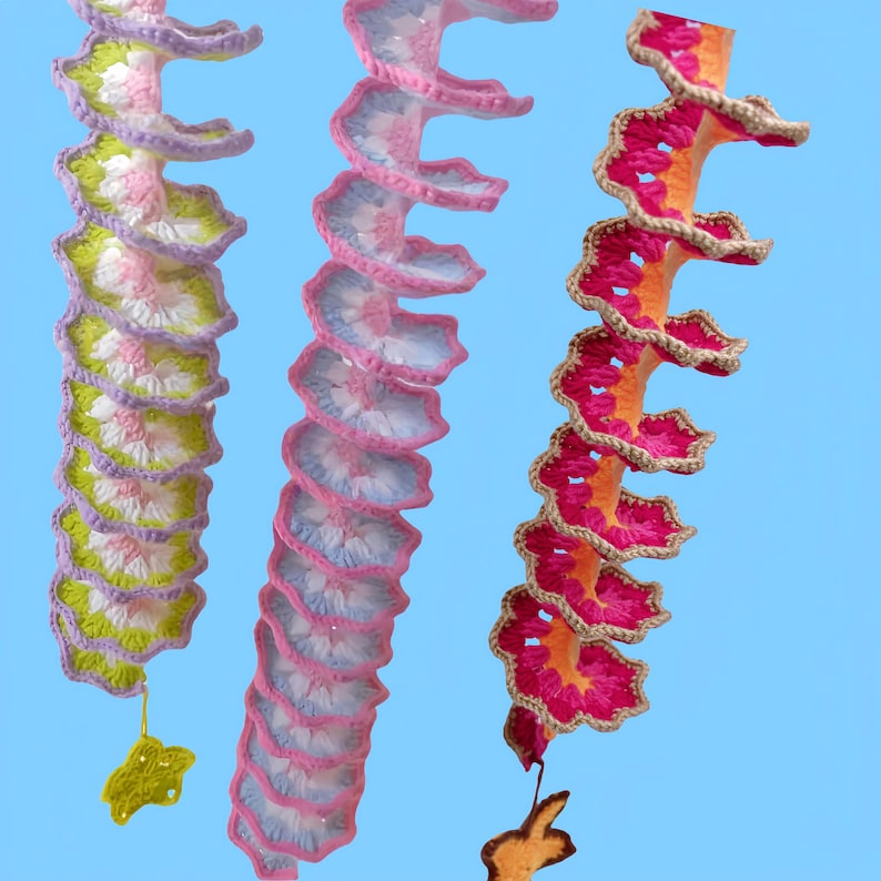 May include: Three colorful, spiral-shaped crochet decorations. The left one has green, pink, and purple accents, the middle one has pink and blue, and the right one has orange and pink. Each has a small, decorative element at the bottom.