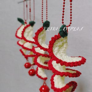 May include: Crocheted spiral ornaments with red and white detailing, accented with green leaves and red ball pendants. The text "I LIKE RIPPLES" is visible. These handmade decorations are likely for holiday or seasonal use.