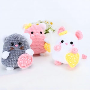 May include: Three crocheted plush toys shaped like mice. The mice are holding hearts in their paws. One mouse is gray, one is pink, and one is white.