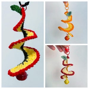 May include: Crocheted spiral-shaped toy in yellow, red, and green, with a small red ball at the bottom and a black ring at the top. The toy is designed with a spiral shape and a bell at the bottom.