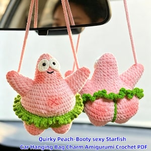 May include: Two pink crocheted starfish figures hanging from strings. Each figure features a light pink body, white eyes with black pupils, and a green ruffled skirt around the waist. The figures are displayed as car hanging ornaments.