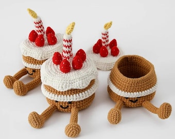 Puede incluir: Tres recipientes de crochet con forma de pastel con caras sonrientes y piernas. Cada pastel tiene una base de glaseado blanco con decoraciones de caramelo rojo y blanco y una vela amarilla.