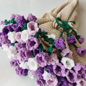 May include: A crocheted flower bouquet with purple, white, and pink flowers. The bouquet is made of yarn and has green stems.