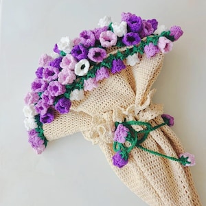 May include: A crocheted garment with a floral design. The garment is beige with purple, pink, and white flowers. The flowers are crocheted and have green leaves.