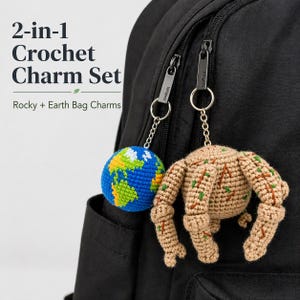 May include: A 2-in-1 crochet charm set featuring a blue and green globe charm and a tan, brown, and green creature charm. The charms are attached to a black backpack with silver-colored chains and key rings. The text "2-in-1 Crochet Charm Set" is visible.