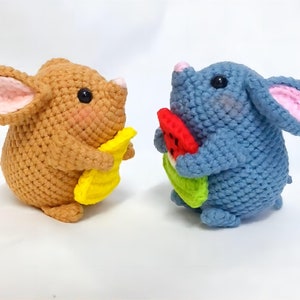 May include: Two crocheted mouse plushies holding fruit. The brown mouse is holding a yellow banana and the blue mouse is holding a red watermelon.