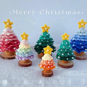 May include: Six crocheted Christmas trees in various colors, including pink, green, blue, and rainbow, with yellow star toppers and pearl embellishments.  "Merry Christmas" is written in white text on a light blue background.