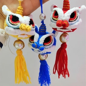 May include: Three crocheted lion dance head ornaments with yellow, blue, and red tassels. Each ornament has a pearl bead and a gold cord.