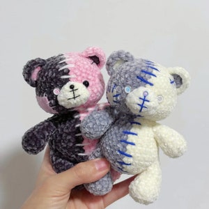 May include: Two crocheted teddy bears, one with pink and black yarn and the other with white and blue yarn. Both bears have stitched details that resemble stitches.