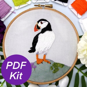 Könnte beinhalten: Ein PDF-Stickset mit einem farbenfrohen Papageientaucher-Motiv. Das Set enthält einen Stickrahmen, Stoff und Stickgarn.