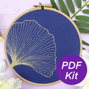 May include: A gold metallic embroidery design of a ginkgo leaf on a dark blue fabric stretched in a wooden embroidery hoop. The text "PDF Kit" is on a purple circle.
