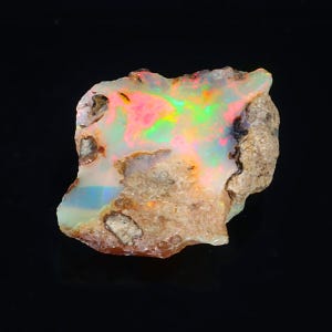 Peut inclure: Un opale brut naturel avec un éclat irisé coloré. L'opale est de couleur brun clair avec des taches de vert, bleu, rose et jaune.