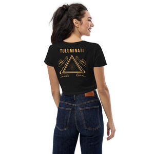 Puede incluir: Camiseta negra de corte corto con un gr&aacute;fico dorado de un ojo dentro de un tri&aacute;ngulo con manos a cada lado. El texto "TULUMINATI" est&aacute; por encima del gr&aacute;fico.