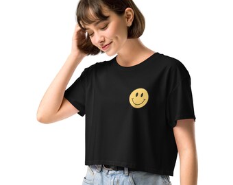 Puede incluir: Camiseta negra de corte corto con un gráfico de cara sonriente amarilla.