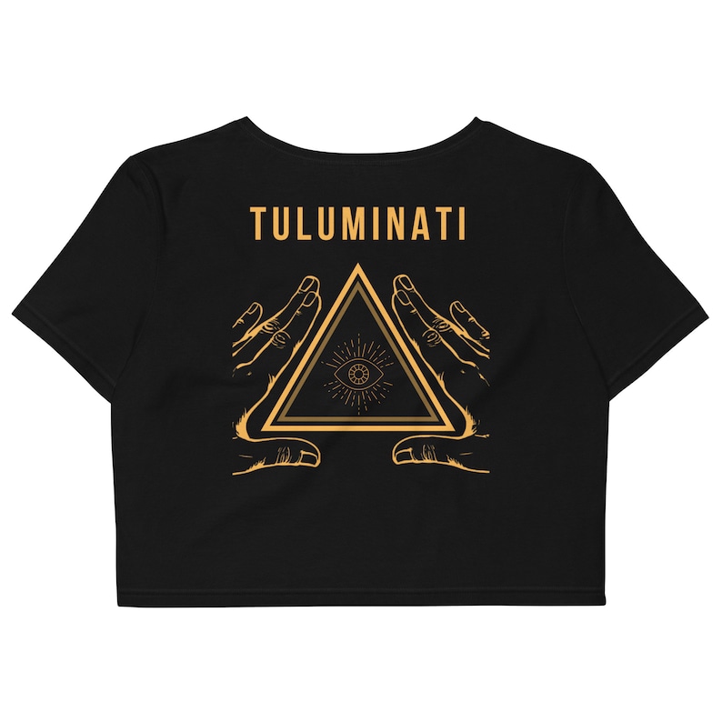 Puede incluir: Crop top negro con un gr&aacute;fico dorado de un tri&aacute;ngulo con un ojo dentro, rodeado de dos manos. El texto "TULUMINATI" est&aacute; por encima del gr&aacute;fico.