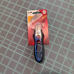 May include: Kai thread clips in original packaging, measuring 4 3/4 inches. The tool features a silver metal blade section with a clear plastic safety cap and a black and blue ergonomic handle. The packaging is red and white with black text.