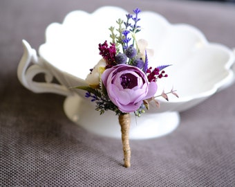 Op de afbeelding: Een klein boeket van paarse, witte en bordeauxrode kunstbloemen met een jute steel. Het boeket ligt op een witte keramische kom.
