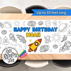May include: A white, space-themed colouring table runner with the text "HAPPY BIRTHDAY NOAH". The runner features a yellow and red rocket, planets, astronauts, and stars. Includes a set of coloured markers. The banner is up to 3 metres long.