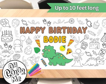 Op de afbeelding: Een witte kleurtafelonderlegger met een dinosaurus thema. Het heeft een groene dinosaurus, een verjaardagsslogan die zegt "Happy Birthday Bodie", en andere dinosaurus-thema illustraties. De onderlegger is tot 3 meter lang en bevat een set gekleurde stiften.