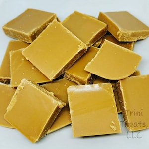 May include: A close-up of a pile of golden brown fudge squares. The fudge is arranged in a random pattern on a white surface. The text "Trini Treats, LLC" is visible in the lower right corner of the image.