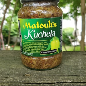 May include: A glass jar of Matouk's Kuchela, a blend of unripened mangoes, East Indian spices, and West Indian peppers. The label reads "This exotic blend of unripened mangoes, East Indian Spices and West Indian peppers, provides a mouth watering dimension to any recipe. A traditional condiment with Curries and Tandoories. Excellent with bean salads, cold dips, poultry and rice dishes." The jar has a net weight of 13.5 oz (380g).