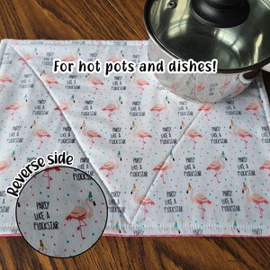 May include: White cotton pot holder with a pink flamingo pattern and the text "Party Like A Flockstar" on the reverse side. The pot holder is quilted and has a pink binding. The pot holder is on a wooden surface with a silver pot on top of it.