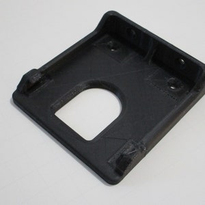 May include: Black plastic 3D printed wall mount with a rectangular opening and three holes.