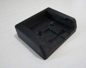 May include: A black plastic 3D printed mount with two holes for screws. The mount has a rectangular shape with a raised lip on one side.