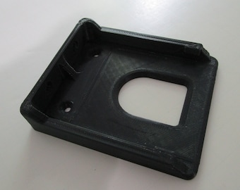 May include: A black 3D printed plastic mount with a rectangular opening. The mount has a raised lip on the top and two small holes on the side.