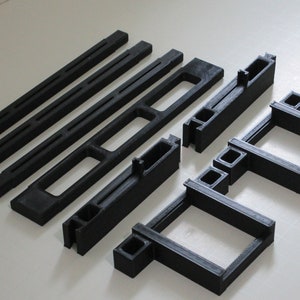 Könnte beinhalten: Ein Satz schwarzer Plastikteile zum Bau eines Modells. Die Teile sind in verschiedenen Längen und haben Schlitze und Löcher zum Verbinden.